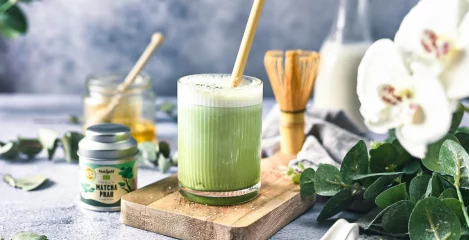 Matcha in einem durchsichtigen Becher, umgeben von Getränkezutaten