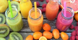 Orangefarbener, grüner und rosa Smoothie, umgeben von Früchten auf einem Holztisch