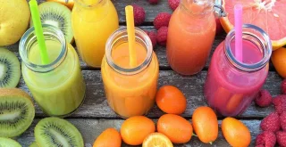 Orangefarbener, grüner und rosa Smoothie, umgeben von Früchten auf einem Holztisch