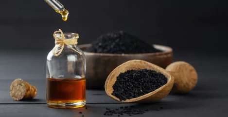 Schwarzkümmelöl aus einer Pipette mit Samen in einem Holzlöffel