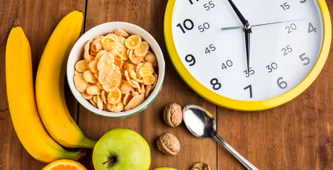 Lebensmittel und eine Uhr, die auf einem Tisch mit Obst und Cornflakes steht.