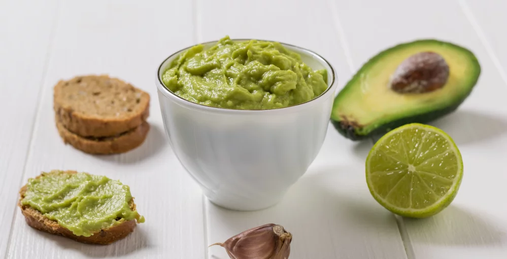 Auf dem Tisch eine Schale Guacamole mit Avocado und Brot